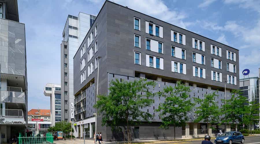 Modern B&B Hotel building with dark facade in a city street with trees and traffic.