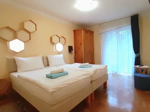 Twin beds with white linens in a guest room with honeycomb wall lights and wooden wardrobe.