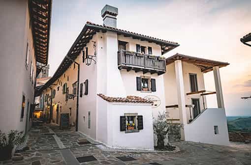 Narrow stone alley between white stucco buildings with terracotta roofs at dusk.