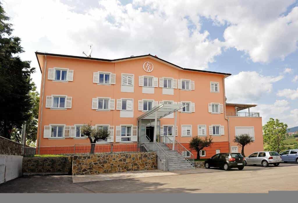 Hotel Kozana building with peach facade, white shutters, and exterior staircase under cloudy sky.
