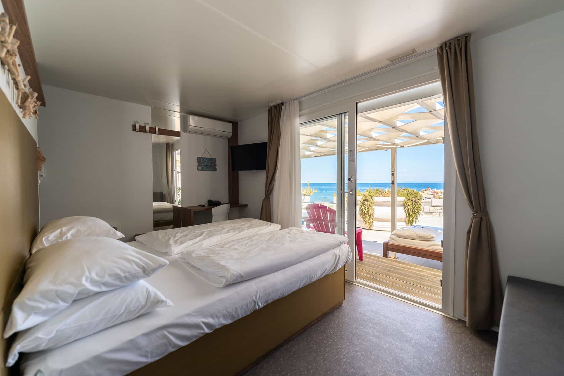 Bedroom with twin beds opening onto a deck overlooking the bright blue sea.