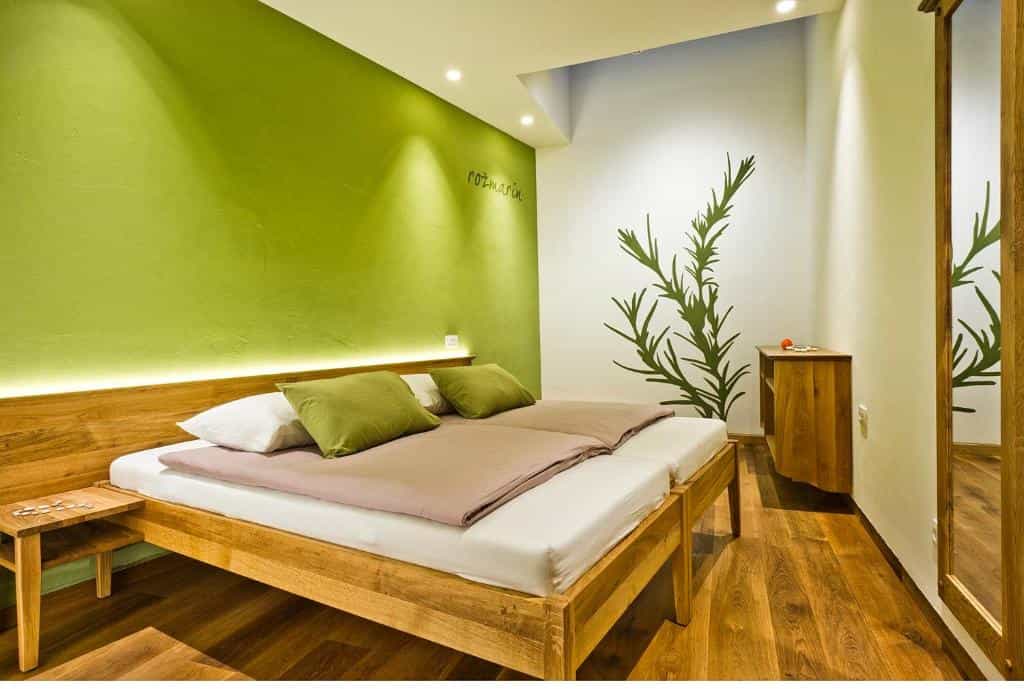 Twin beds with wooden frame, green accent wall, and rosemary wall decal in a room.