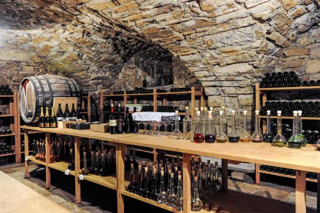 Wine cellar with stone vaulted ceiling, wooden racks, barrel, and bottles on tasting table
