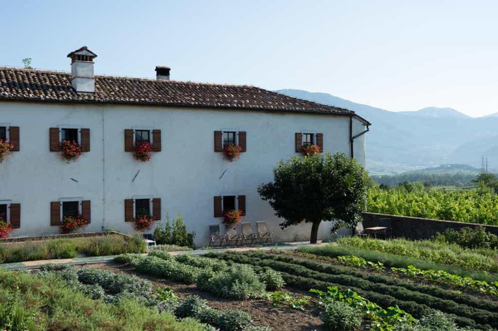 White farmhouse with flower boxes, herb garden, and mountains in background