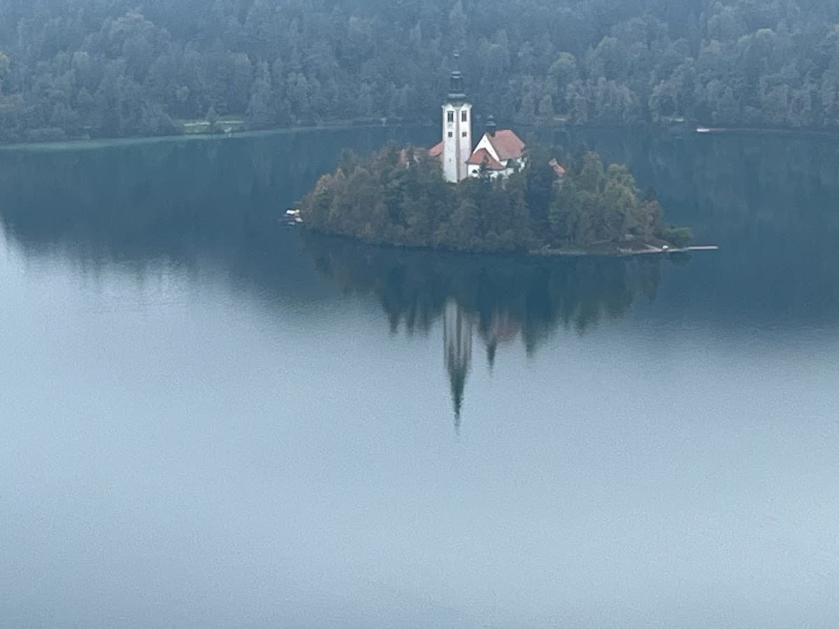 Church on island in Lake Bled reflecting on calm water surrounded by forest