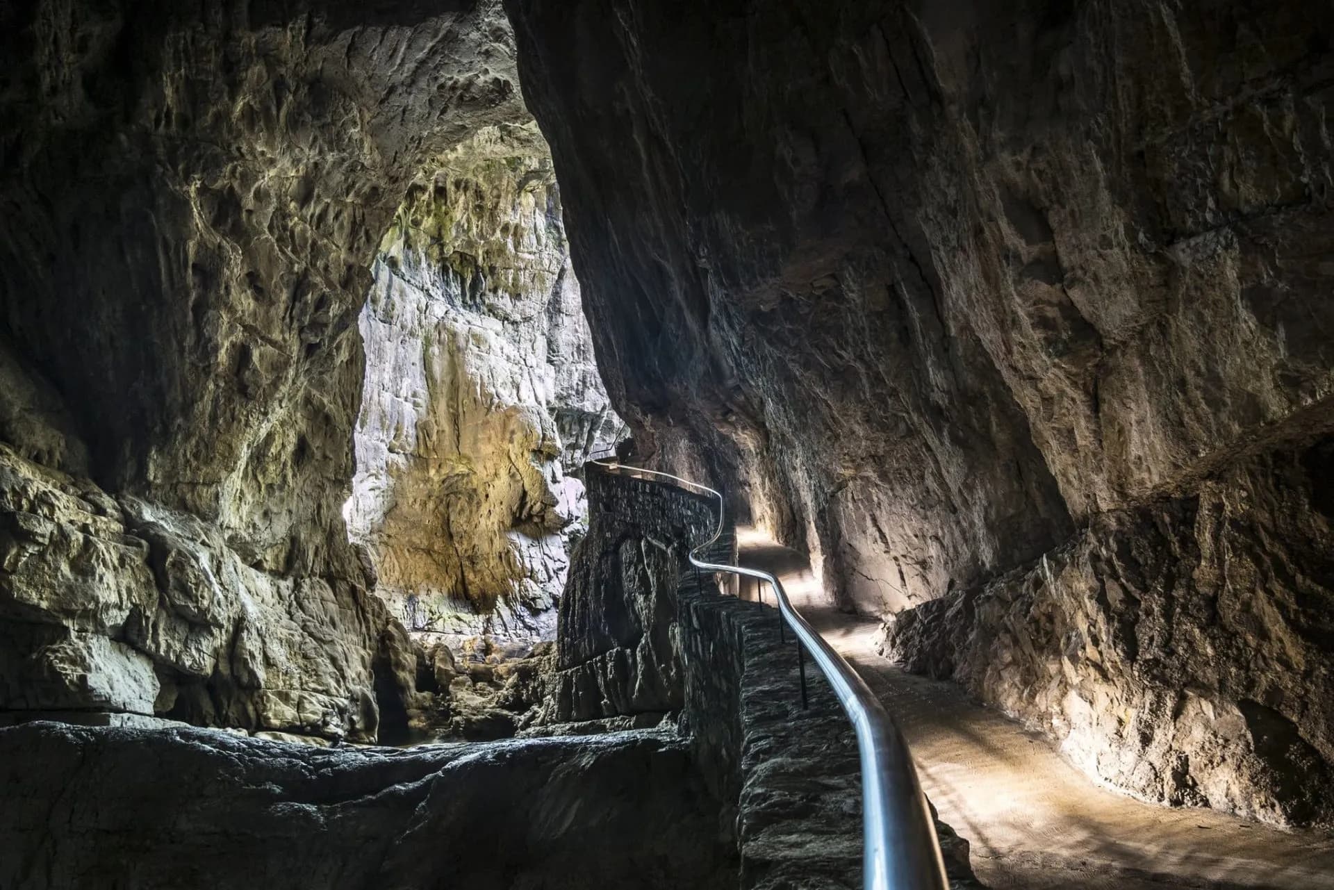 Pathways with metal railing winding through the massive, illuminated caverns of Skocjan Caves.