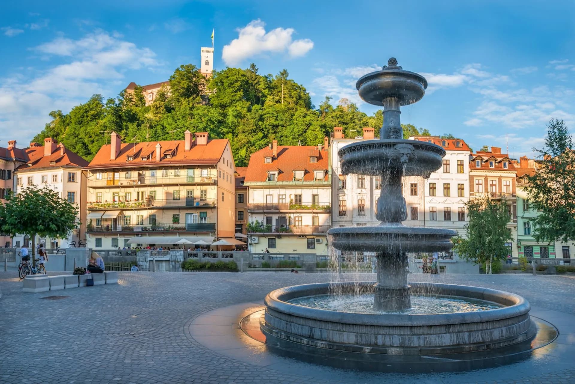 Fountain in Ljubljana City Center square with buildings and Ljubljana Castle on a hill.