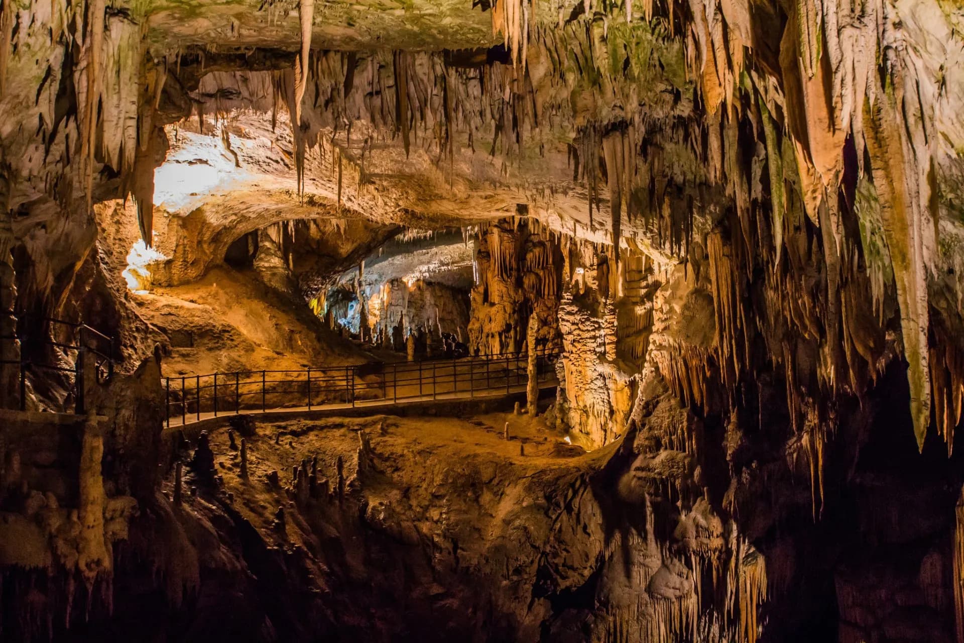Cave interior with stalactites, illuminated walkway, and karst formations at Škocjan Caves.