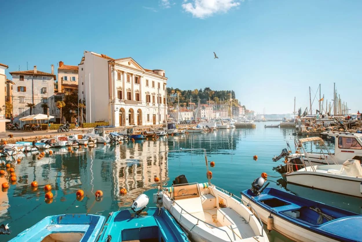 Boats moored in Piran marina with historic white building reflecting in turquoise water