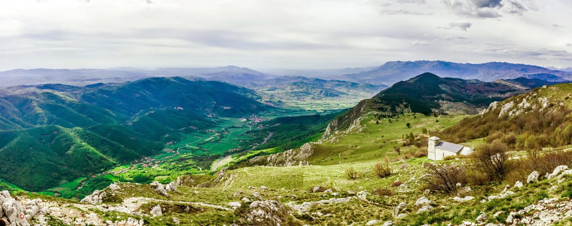 Vipava Valley landscape with green mountains, valley floor, and small white church on hillside.