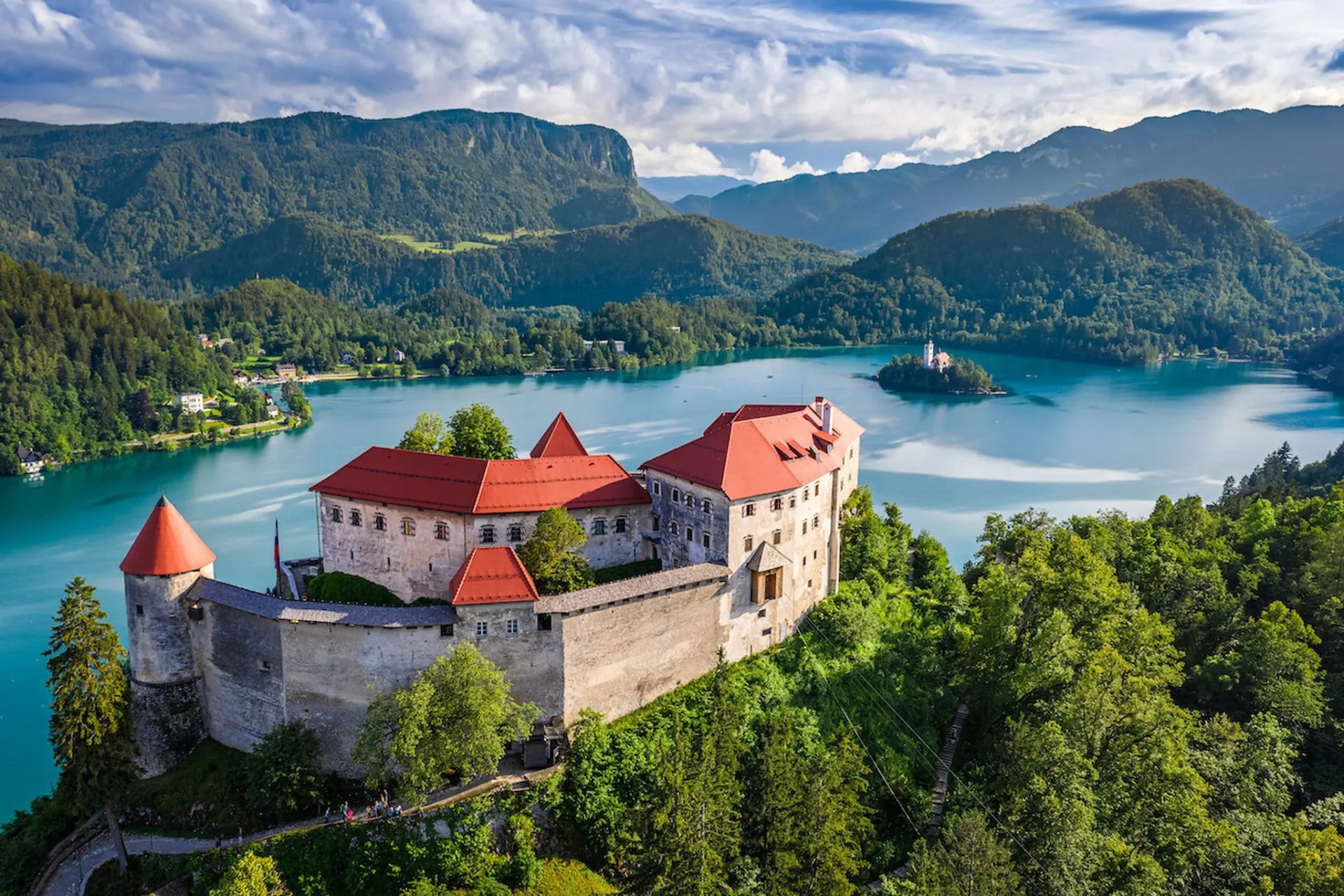 Bled Castle above turquoise lake with island church and forested mountains in Slovenia