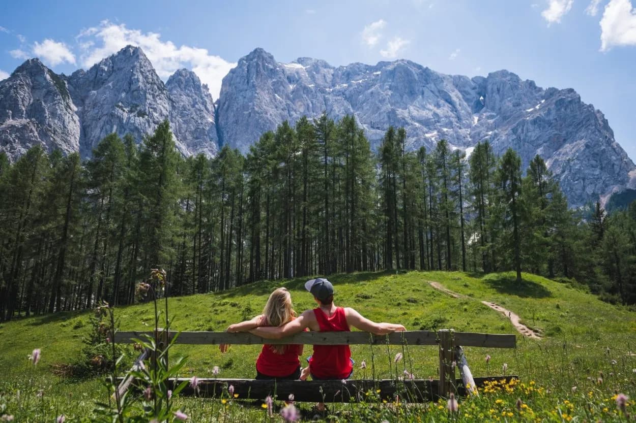 Couple relaxing on bench overlooking Vrsic Pass mountains and pine forest
