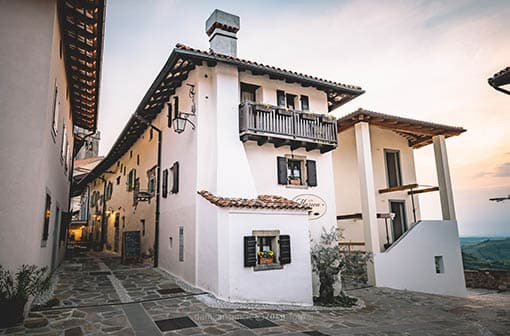 Narrow stone alley between white stucco buildings with terracotta roofs at dusk.