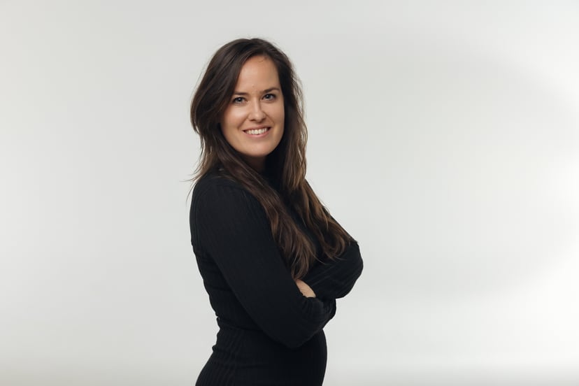 Smiling woman with long brown hair wearing a black long-sleeved shirt against a white background.