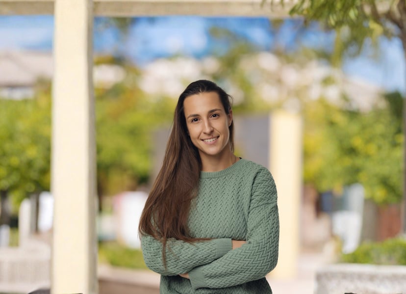 Smiling woman with long brown hair wearing a green sweater standing outdoors.